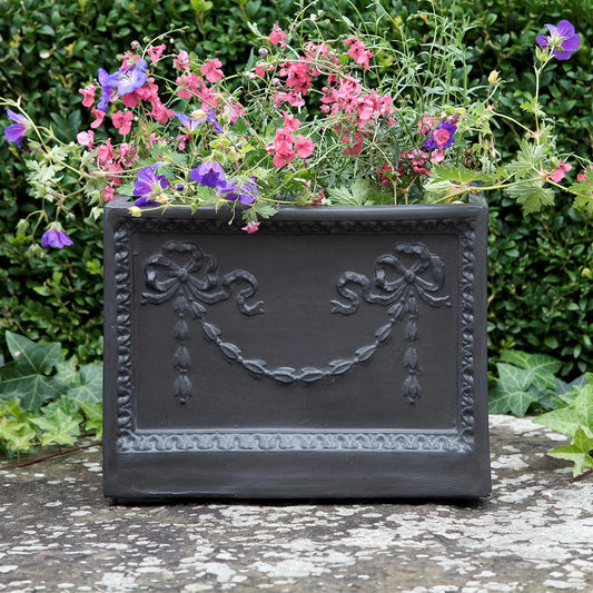 Decorative black planter with flowers against a green hedge background